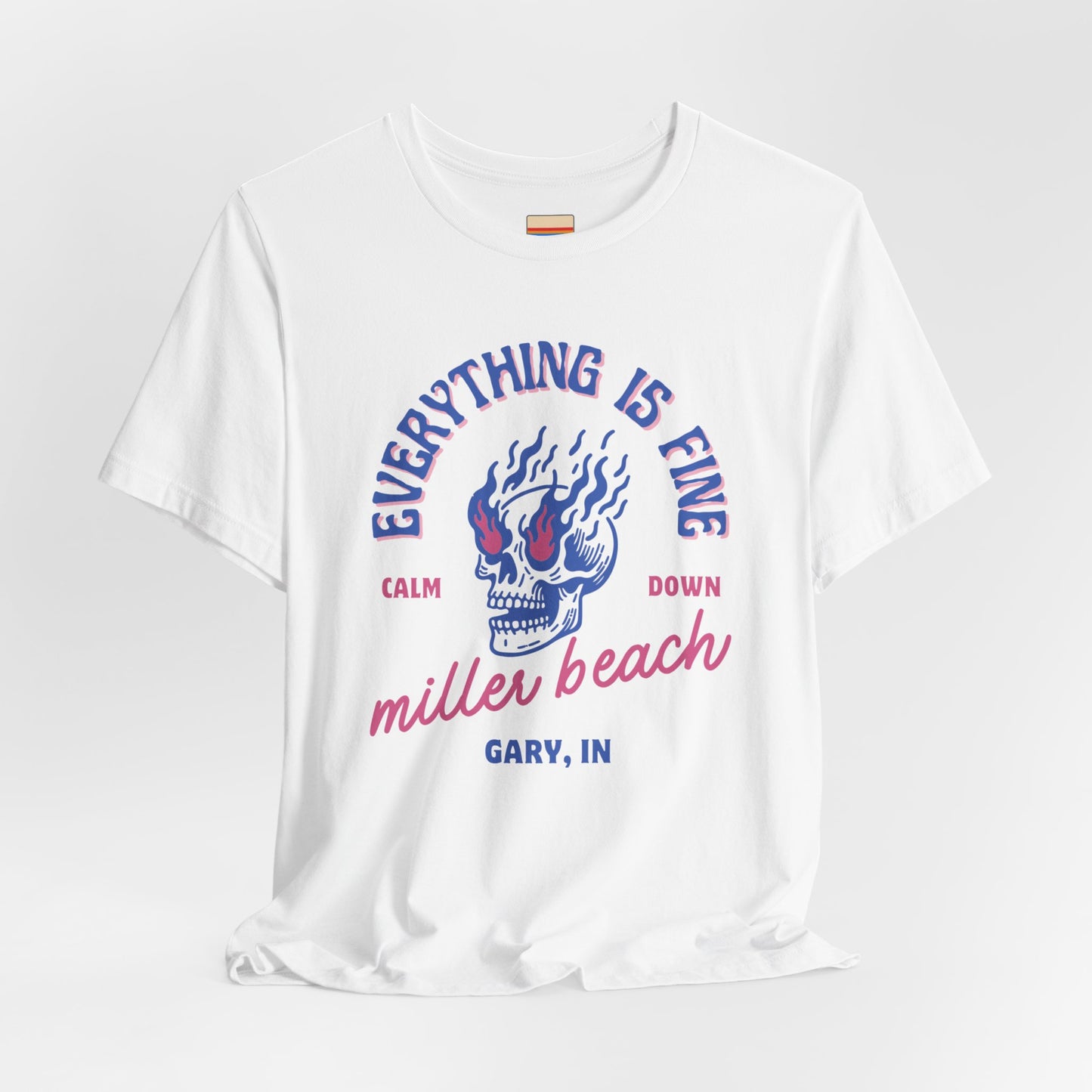 The Miller Beach Calm Down Everything is Fine - Unisex Jersey Short Sleeve Tee from Printify, crafted from soft Airlume combed cotton, showcases a peach-colored design with a flaming skull in the center. Above the design, it reads "Everything is fine," and below it says, "Calm down Miller Beach." In smaller text at the bottom, it reads "Gary, IN.