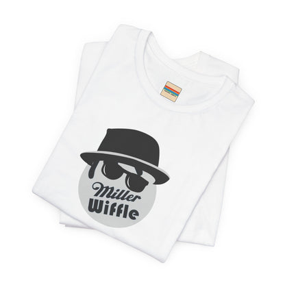 A purple unisex jersey tee from Printify, named the "Miller Wiffel Ball - Blues Brothers - Unisex Jersey Short Sleeve Tee," features a stylized graphic of a ball wearing a black fedora and sunglasses with the text "Miller Wiffel" below it. Another identical soft cotton t-shirt is neatly folded underneath, highlighting its breathable fabric.