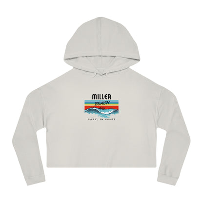 Introducing the Miller Beach Surf Women's Cropped Hooded Sweatshirt by Printify, a white personalized hoodie featuring a pastel tie-dye pattern. The front showcases a bold "Miller Beach" graphic above "Gary, IN" on a vibrant striped background with stylized mountains and waves. This long-sleeve hoodie comes in a trendy cropped style complete with a drawstring hood.