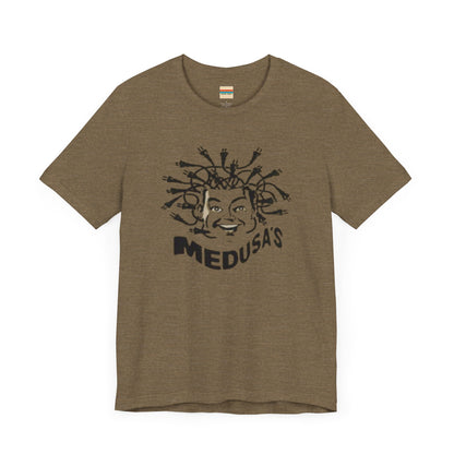 A cream-colored unisex jersey short sleeve tee from Printify, titled "Medusa's 1980s Dance Club Chicago," features a black and white illustration of a cartoonish Medusa head. The soft cotton design showcases numerous snakes as hair with a smiling face. Below, the word "MEDUSA'S" is printed in bold, playful font.