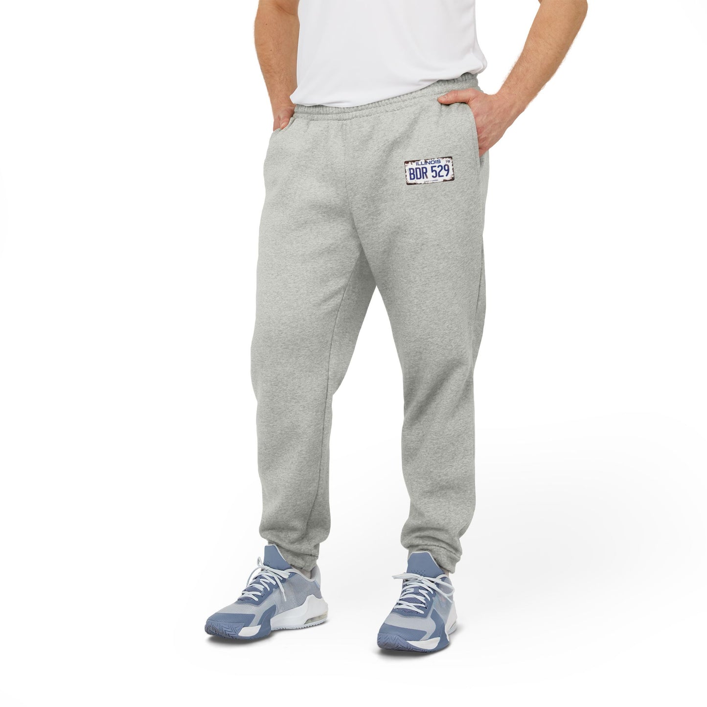 These gray fleece joggers by Printify, named "Blues Brothers License Plate - BDR529 - Adidas Fleece Joggers," feature an iconic Adidas logo on the left thigh and a patch with "BDR529" on the right thigh, evoking retro movie nostalgia. Designed with an elastic waistband and cuffs, these joggers offer both style and comfort.