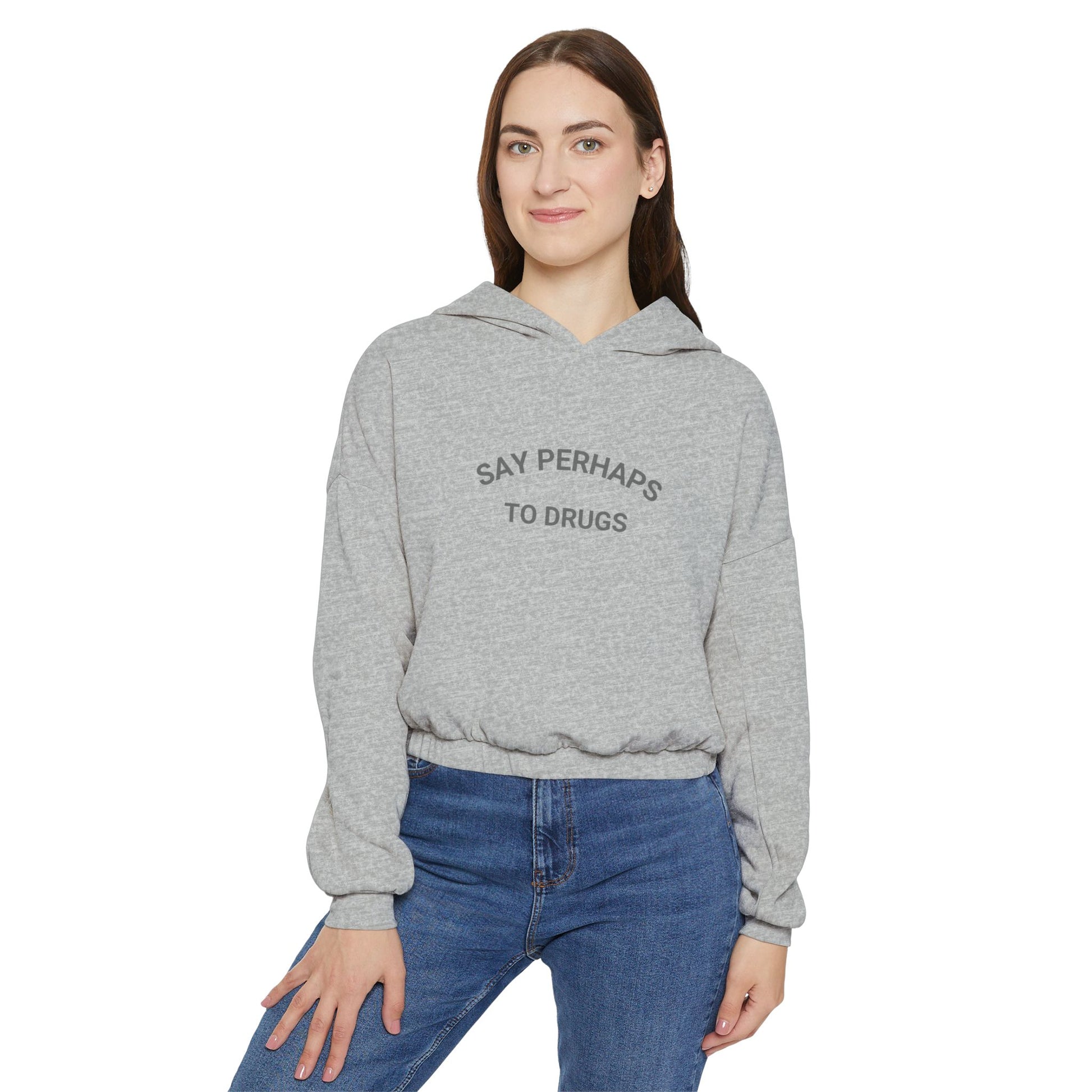 A person confidently stands in front of the camera with one hand on their hip, wearing a Printify "Say Perhaps to Drugs" Women's Cinched Bottom Hoodie. Crafted from soft Airlume cotton, this light-colored cropped hoodie pairs stylishly with blue jeans.