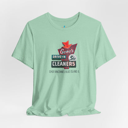 A unisex Jersey short sleeve tee from Printify featuring a light grey color with a retro-style graphic in the center. The design showcases text that reads "Gene's Drive In Cleaners, 5th," along with the address "12401 Vincennes Blue Island IL" in a blend of vintage fonts and colors, evoking the classic Chicago Fire-era vintage sign aesthetic.