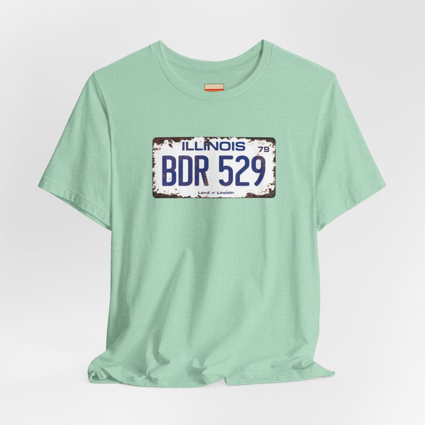 The Printify Blues Brothers BDR 529 License Plate Unisex Jersey Short Sleeve Tee showcases a vintage Illinois license plate graphic with "BDR 529" prominently displayed, as famously seen in the Blues Brothers film. The design includes "Illinois" and "Land of Lincoln" above and below the numbers, with a weathered, rustic look that enhances its retro appeal.