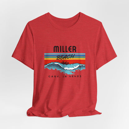 The Miller Beach 46403 Surf Style - Unisex Jersey Short Sleeve Tee by Printify features a retro surf-inspired design on a yellow background. The shirt displays "MILLER BEACH" above waves with a skyline illustration, while "Cary, IN 46403" is printed below the waves. The vibrant design also includes colorful stripes in shades of blue, red, and orange.