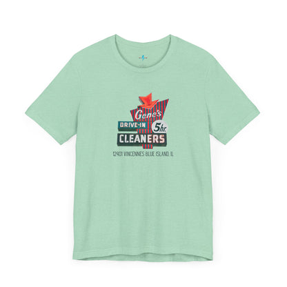 A unisex Jersey short sleeve tee from Printify featuring a light grey color with a retro-style graphic in the center. The design showcases text that reads "Gene's Drive In Cleaners, 5th," along with the address "12401 Vincennes Blue Island IL" in a blend of vintage fonts and colors, evoking the classic Chicago Fire-era vintage sign aesthetic.