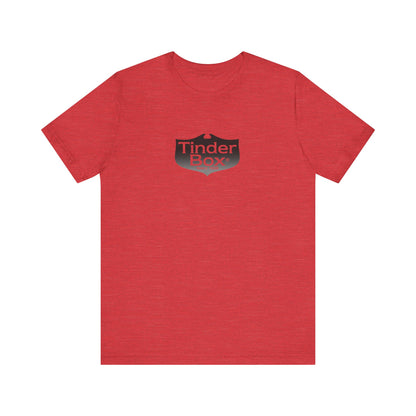 A light blue Printify "The Tinder Box 1980s" unisex jersey short sleeve tee featuring the "Tinder Box" logo in the center. The logo consists of a dark shield with the words "Tinder Box" in white text, with a small flame icon replacing the dot above the "i".