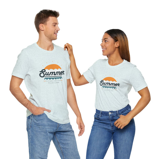 A man and a woman stand smiling at each other, both wearing matching Miller Beach is Hard Summer Unisex Jersey Short Sleeve Tees by Printify in light gray. The tees feature a sunset design with the word "Summer." The man has his hand in his pocket while the woman touches his shoulder. They both wear blue jeans, enjoying the soft cotton feel of their shirts.