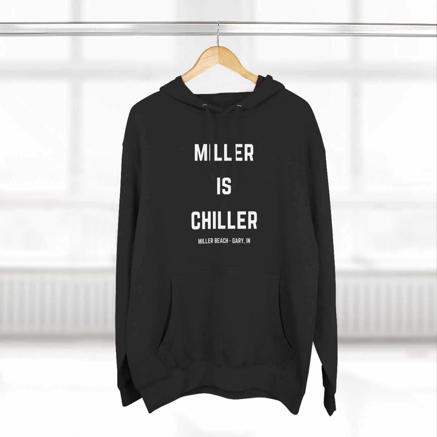 The Miller is Chiller - Miller Beach Three-Panel Fleece Hoodie from Printify features bold white text reading "MILLER IS CHILLER" on the front, with smaller text below stating "MILLER BEACH - GARY, IN." This comfortable black hoodie includes a front pocket and drawstrings.