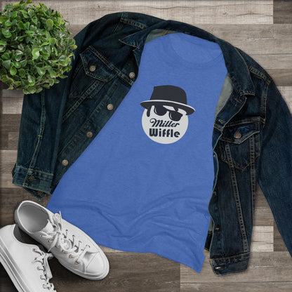 A cozy red t-shirt, the Miller Wiffel Ball - Blues Brothers - Women's Triblend Tee by Printify, features a graphic of a masked face wearing a fedora hat and sunglasses, along with the text "Miller Wiffle." The t-shirt is displayed on a wooden floor, paired with a denim jacket, white sneakers, and a potted green plant to create a vintage look.