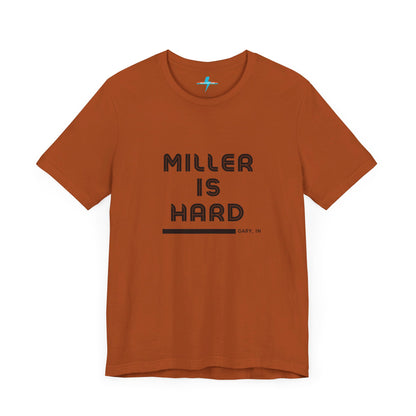 A unisex jersey short sleeve tee from Printify in burnt orange features the bold black text "MILLER IS HARD" on the chest, with "GARY, IN" written beneath in smaller black font. Perfect for showcasing Miller Beach's iconic spirit, this t-shirt is displayed against a plain white background.