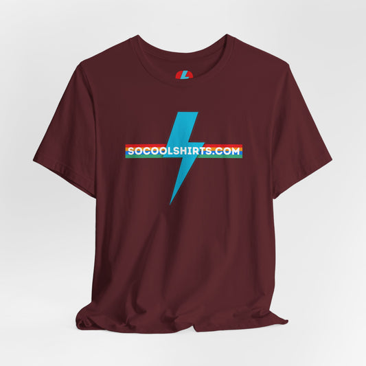 This unisex jersey short sleeve tee by Printify features a striking maroon color with a central light blue lightning bolt design. The text "SOCOOLSHIRTS.COM" is prominently displayed across the lightning bolt in white letters, set against a multicolored background that exudes retro vibes. The shirt is shown laid flat on a white backdrop.