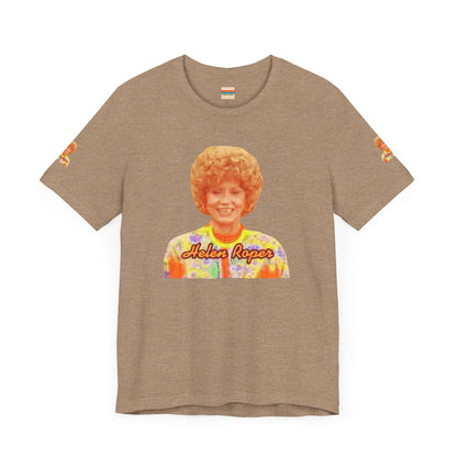 A lavender-colored Helen (Mrs.) Roper Three's Company - Unisex Jersey Short Sleeve Tee by Printify is hanging on a wooden hanger against a white background. This T-shirt features an image of a smiling person with curly hair wearing a colorful blouse, with the text "Helen Roper" underneath the image. Both sleeves have identical designs, making it perfect Three's Company merchandise.