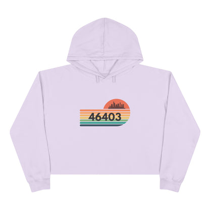 The Miller Beach 46403 Women's Crop Hoodie by Printify features a nostalgic design with a city skyline silhouette and the iconic "46403" zip code, set against a striped sunset backdrop in vibrant orange, green, and yellow hues that capture the essence of Miller Beach.