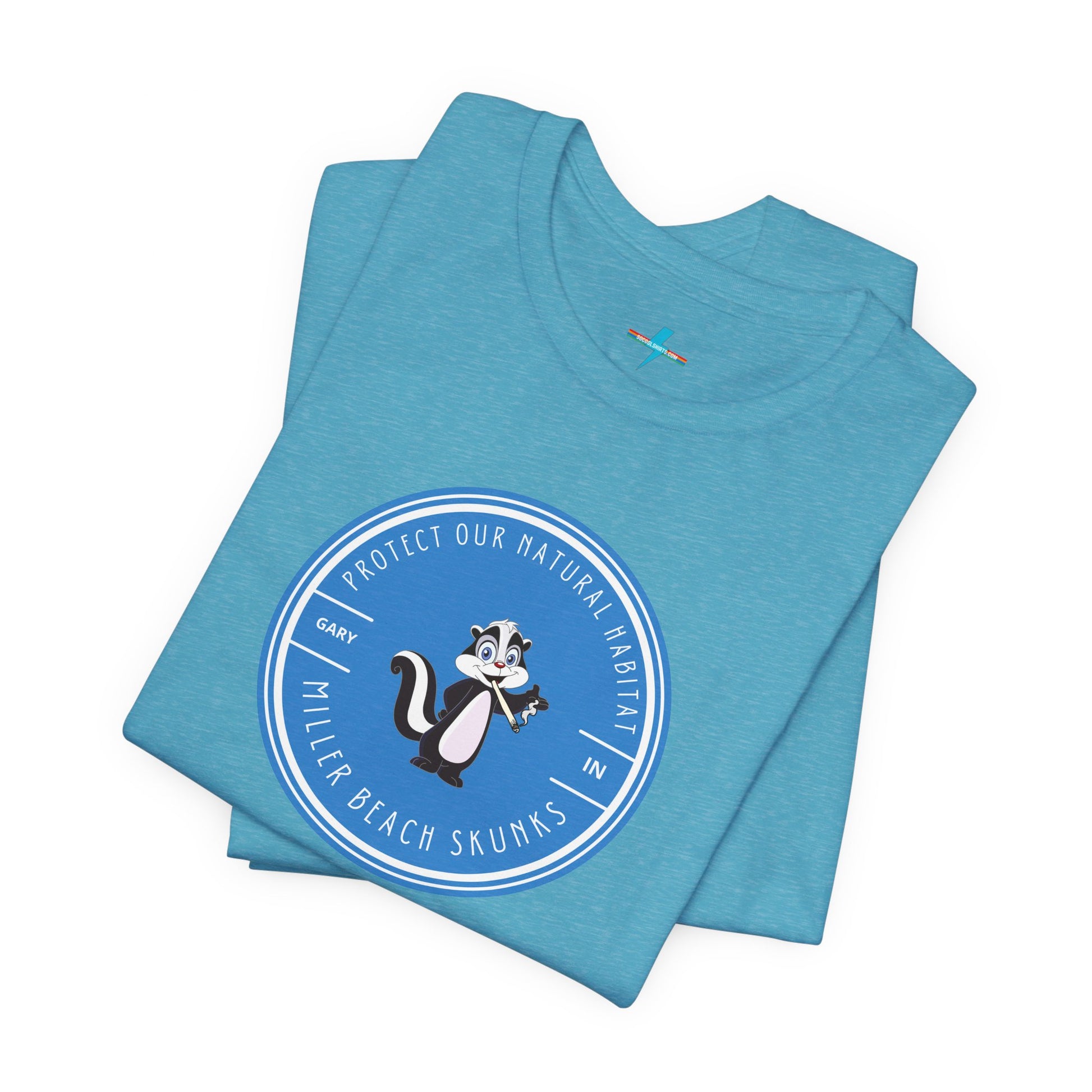 The Printify Miller Beach Skunks - Unisex Jersey Short Sleeve Tee is a gray T-shirt that features a circular blue logo at the center. Inside the logo, there is an illustration of a skunk with the text "Protect Our Habitat" and "Miller Beach Skunks" around the border, promoting environmental consciousness. The upper left part of the logo reads "Gary, IN.