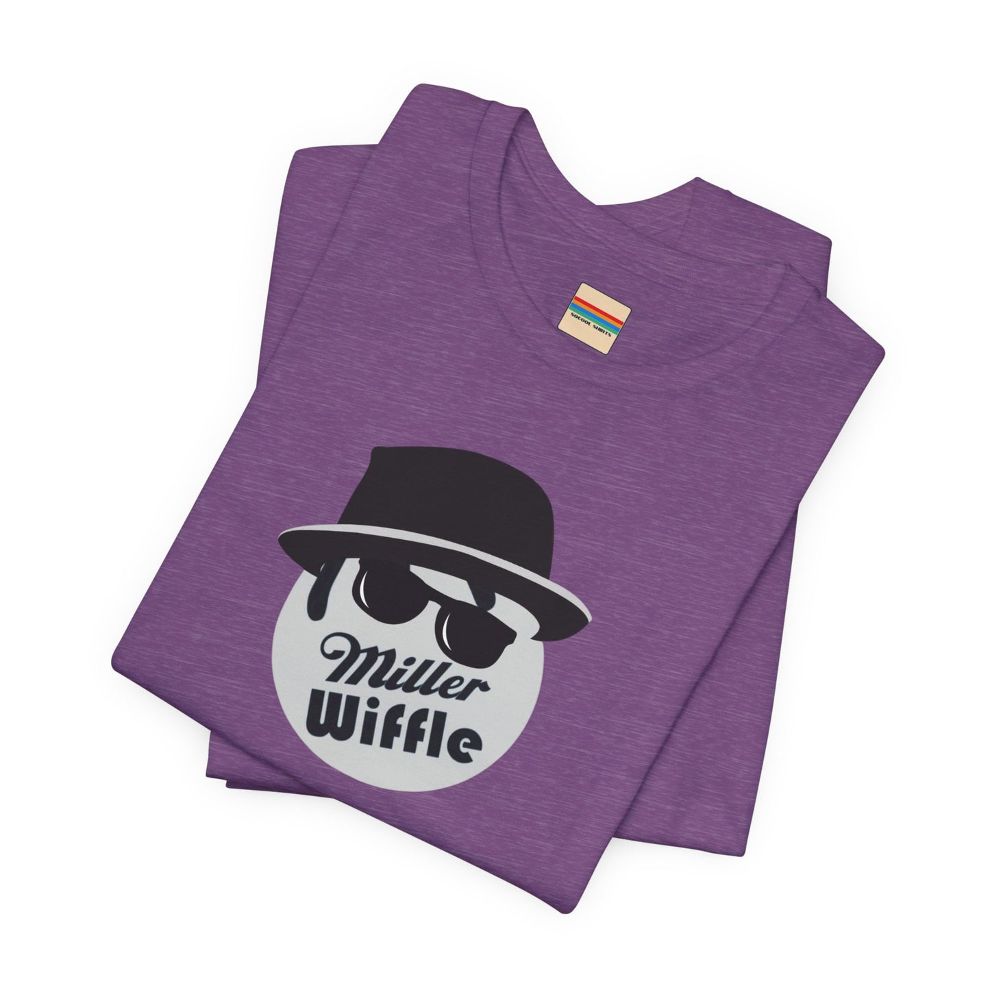 A purple unisex jersey tee from Printify, named the "Miller Wiffel Ball - Blues Brothers - Unisex Jersey Short Sleeve Tee," features a stylized graphic of a ball wearing a black fedora and sunglasses with the text "Miller Wiffel" below it. Another identical soft cotton t-shirt is neatly folded underneath, highlighting its breathable fabric.