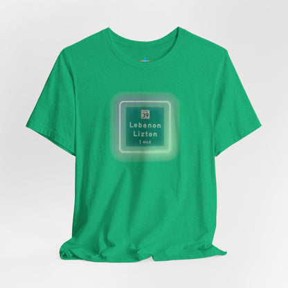 Introducing "The Lebanon Loop - Indiana" unisex jersey short sleeve tee by Printify. This green t-shirt features a graphic of a road sign displaying "39 Lebanon Lizton 1 MILE" within a slightly glowing square frame. It's crafted from 100% Airlume cotton and photographed flat on a white background.