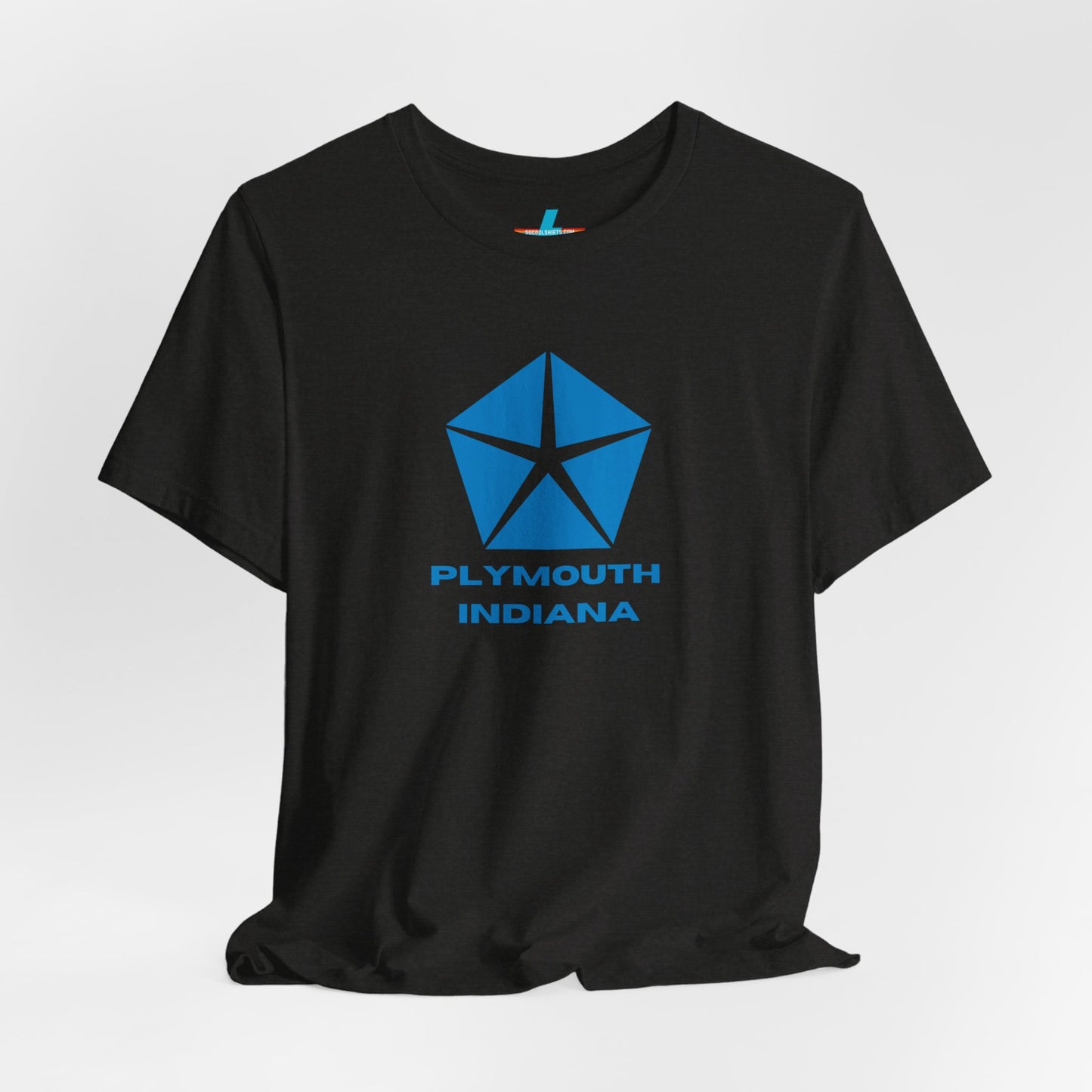 A black Printify Plymouth, Indiana Chrysler Logo T-shirt is displayed against a plain white background. The shirt features a blue, five-point star emblem reminiscent of a vintage autos design above the text "PLYMOUTH INDIANA" in blue, centered across the front. The shirt is laid out flat with the sleeves slightly bent.