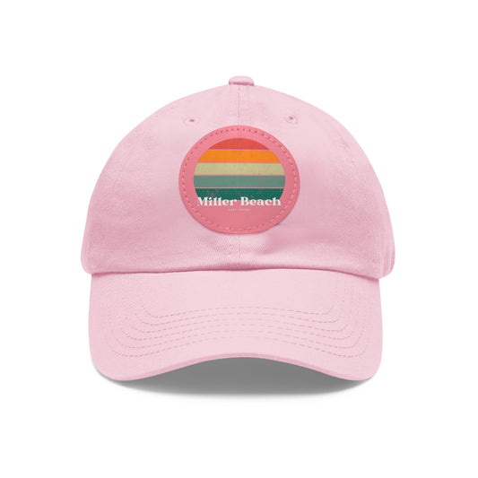 The Miller Beach Retro Sunset - Dad Hat with Leather Patch (Round) by Printify is a pink baseball cap crafted from bio-washed chino twill for added comfort. It features a PU leather patch adorned with horizontal stripes in red, orange, yellow, green, and blue. Below the stripes, "Miller Beach" is embroidered in white. An adjustable strap at the back ensures a perfect fit.