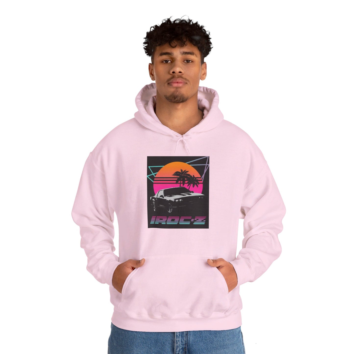 Introducing the Chevrolet IRoc Z28 - 1980s Retro Hoodie by Printify: This vibrant pink hoodie showcases a striking retro design on the front, featuring a classic American muscle car set against an orange and red sunset with palm trees, intersected by geometric shapes. The text "IROCZ" is prominently displayed below the image. Offering a relaxed fit and equipped with a front pocket, this hoodie perfectly captures the essence of 1980s style.