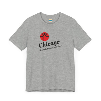 Two gray T-shirts are neatly folded on top of each other, with the top shirt showcasing the text "Chicago Health & Racquetball Clubs" in black below a red logo featuring a person with raised arms inside a circular design. This retro-inspired tee, named "Chicago Health Clubs 1980s Retro - Unisex Jersey Short Sleeve Tee" by Printify, is perfect for any fan of Chicago Health Clubs.