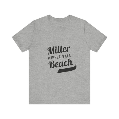 A light blue, soft cotton t-shirt with the text "Miller Beach Wiffel Ball" printed in black on the front. The design features a stylized, curved underline beneath the word "Beach," giving the text a dynamic appearance. This unisex jersey offers a comfortable retail fit for all. Product Name: Miller Beach Wiffel Ball - Unisex Jersey Short Sleeve Tee Retro Logo by Printify.