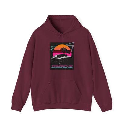 Introducing the Chevrolet IRoc Z28 - 1980s Retro Hoodie by Printify: This vibrant pink hoodie showcases a striking retro design on the front, featuring a classic American muscle car set against an orange and red sunset with palm trees, intersected by geometric shapes. The text "IROCZ" is prominently displayed below the image. Offering a relaxed fit and equipped with a front pocket, this hoodie perfectly captures the essence of 1980s style.