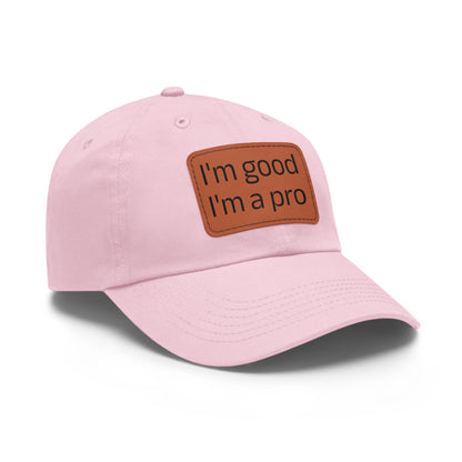 The Printify Dad Hat with Leather Patch (Rectangle) is a black, six-panel low-profile baseball cap made from bio-washed chino twill. This personalized Dad hat features a curved brim, visible stitching details, and a rectangular leather patch on the front that reads "I'm good I'm a pro" in grey text.