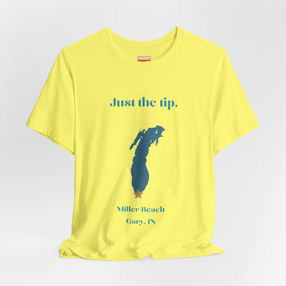 The Just the Tip - Miller Beach Unisex Jersey Short Sleeve Tee by Printify in yellow showcases text and a graphic design. The top displays "Just the tip" above a blue silhouette reminiscent of Indiana. At the bottom, it reads "Miller Beach" and "Gary, IN." Made from soft Airlume combed cotton, this tee offers both comfort and style.