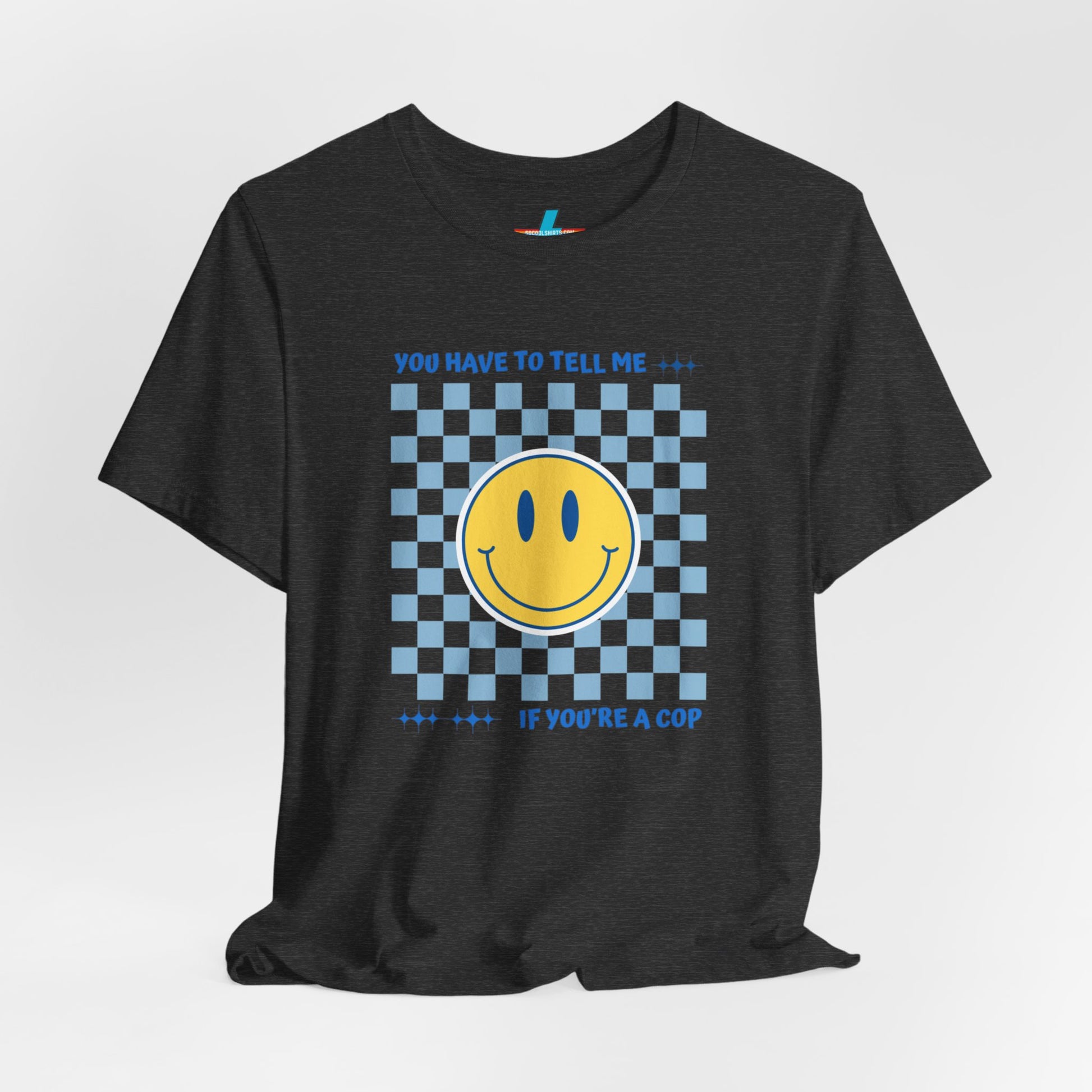 A light yellow unisex jersey short sleeve tee from Printify featuring a blue and yellow checkerboard pattern with a large yellow smiley face in the center. The shirt displays blue text above and below the pattern that reads, "You have to tell me if you're a cop." It's made from 100% Airlume combed and ring-spun cotton.