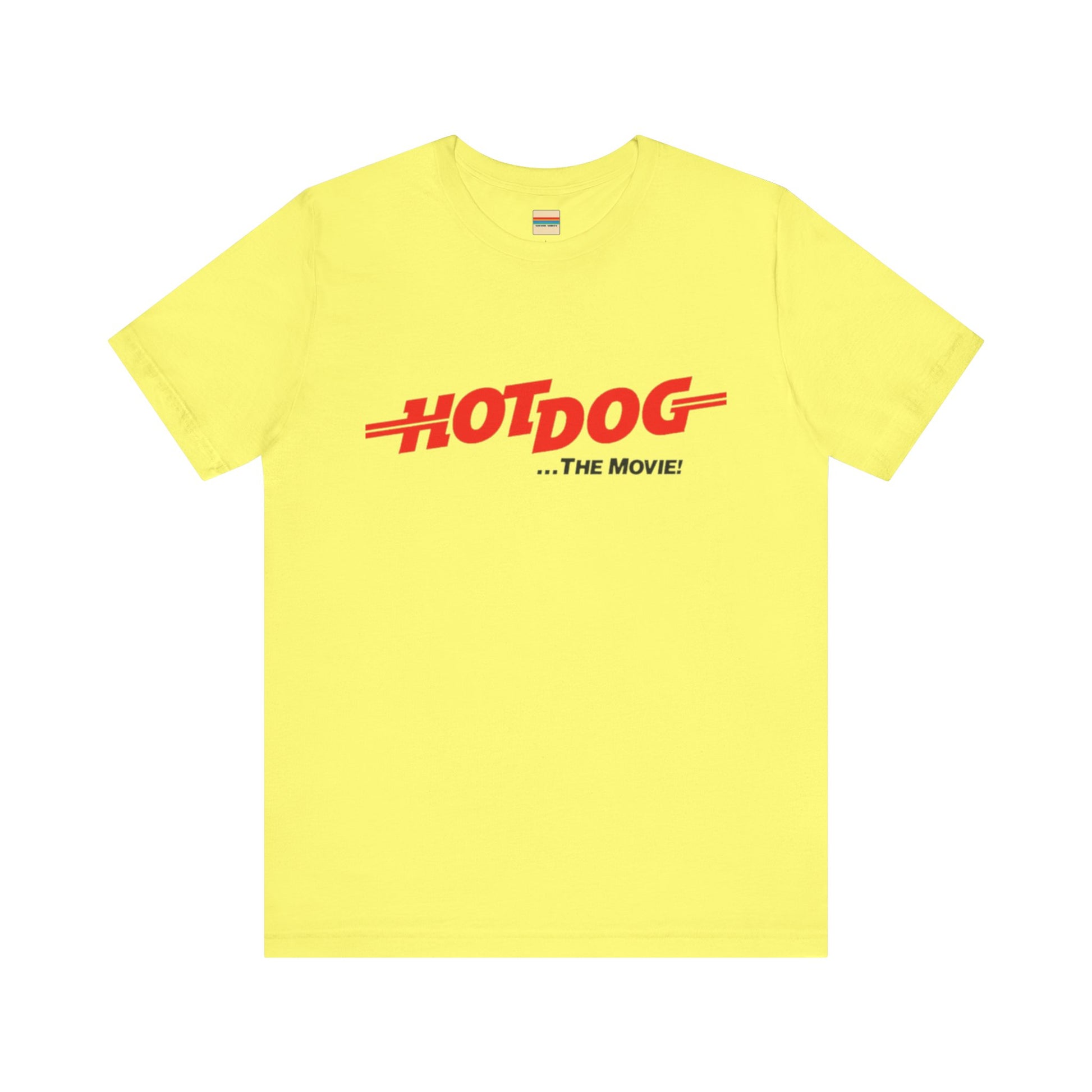 A smiling man and woman interact while wearing matching yellow "Hot Dog The Movie 1984 - Unisex Jersey Short Sleeve Tee" by Printify, featuring bold red "HOT DOG THE MOVIE" text. Their vibrant tees perfectly complement their blue jeans, with the man casually having his hands in his pockets and the woman resting one hand on his shoulder.