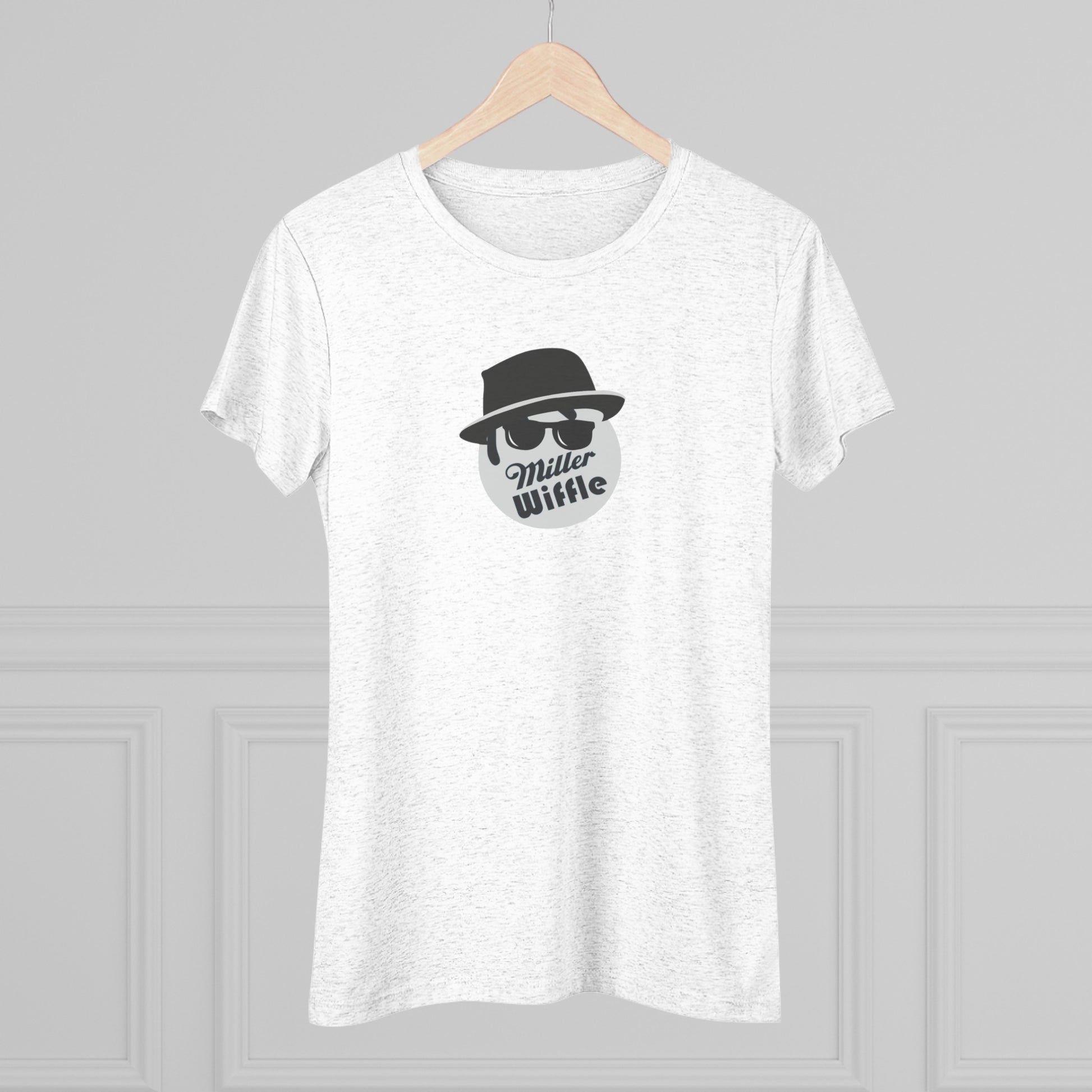 A cozy red t-shirt, the Miller Wiffel Ball - Blues Brothers - Women's Triblend Tee by Printify, features a graphic of a masked face wearing a fedora hat and sunglasses, along with the text "Miller Wiffle." The t-shirt is displayed on a wooden floor, paired with a denim jacket, white sneakers, and a potted green plant to create a vintage look.