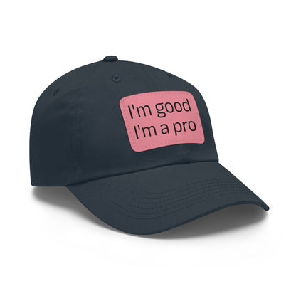 The Printify Dad Hat with Leather Patch (Rectangle) is a black, six-panel low-profile baseball cap made from bio-washed chino twill. This personalized Dad hat features a curved brim, visible stitching details, and a rectangular leather patch on the front that reads "I'm good I'm a pro" in grey text.