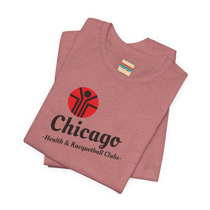 Two gray T-shirts are neatly folded on top of each other, with the top shirt showcasing the text "Chicago Health & Racquetball Clubs" in black below a red logo featuring a person with raised arms inside a circular design. This retro-inspired tee, named "Chicago Health Clubs 1980s Retro - Unisex Jersey Short Sleeve Tee" by Printify, is perfect for any fan of Chicago Health Clubs.