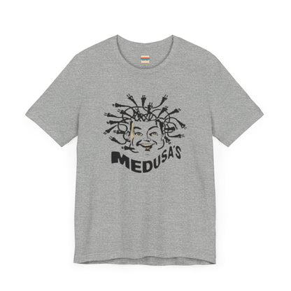 A cream-colored unisex jersey short sleeve tee from Printify, titled "Medusa's 1980s Dance Club Chicago," features a black and white illustration of a cartoonish Medusa head. The soft cotton design showcases numerous snakes as hair with a smiling face. Below, the word "MEDUSA'S" is printed in bold, playful font.