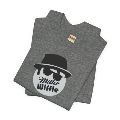 A purple unisex jersey tee from Printify, named the "Miller Wiffel Ball - Blues Brothers - Unisex Jersey Short Sleeve Tee," features a stylized graphic of a ball wearing a black fedora and sunglasses with the text "Miller Wiffel" below it. Another identical soft cotton t-shirt is neatly folded underneath, highlighting its breathable fabric.