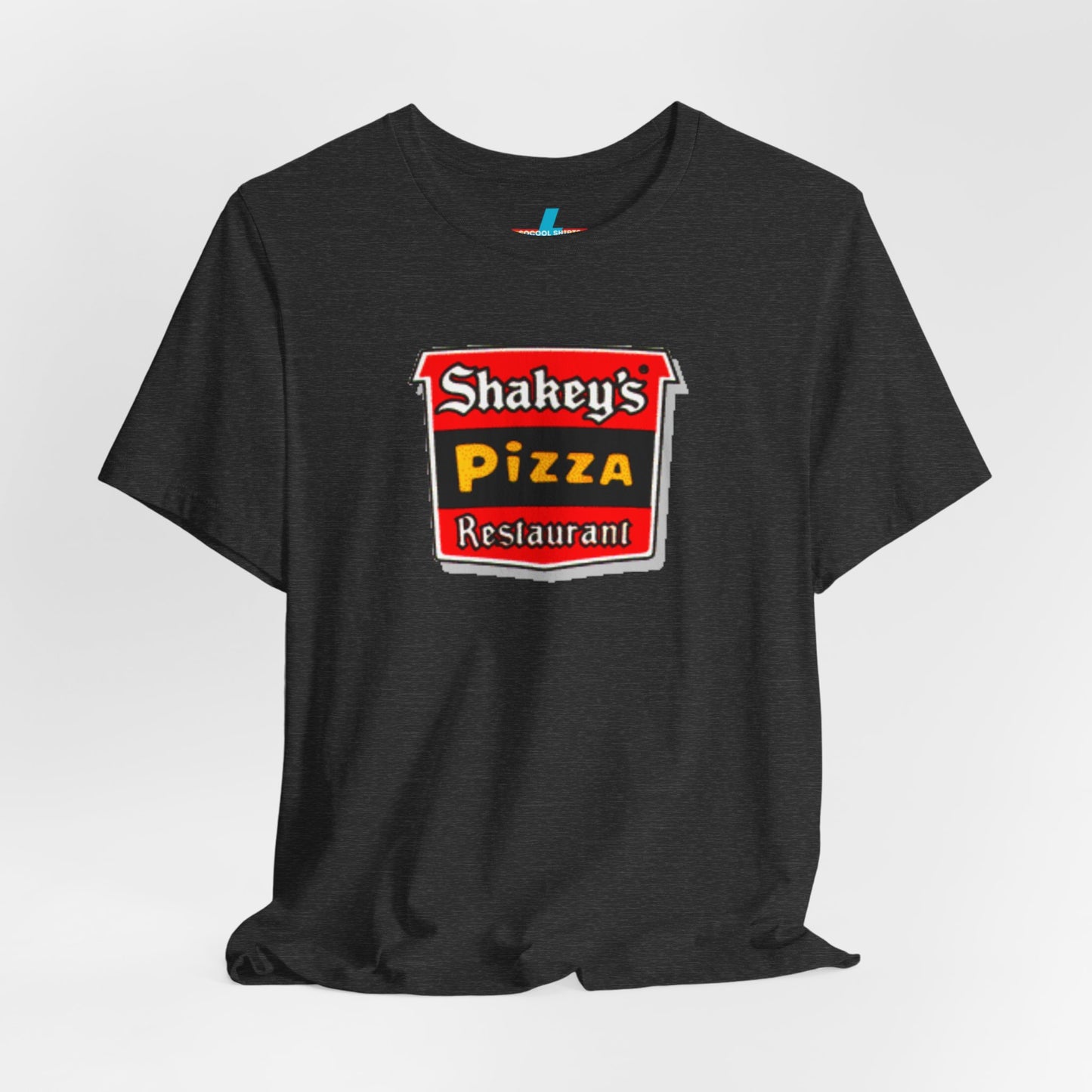 A black Shakey's Pizza - 1980s Retro Logo - Unisex T-Shirt by Printify hangs against a white background. The shirt features a colorful graphic with the text "Shakey's Pizza Restaurant" in white, yellow, and black lettering on a red background, resembling vintage pizza joints signage. This retro tee brings nostalgic vibes of classic pizzerias.