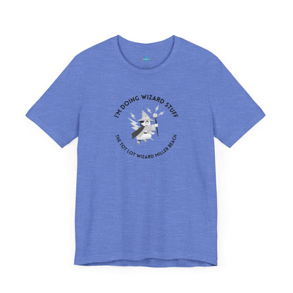 A unisex jersey short sleeve tee in orange from Printify, known as the "Tot Lot Wizard - Miller Beach," features a central graphic of a wizard holding a wand. The design is surrounded by stars and lightning bolts and includes the text "I'M DOING WIZARD STUFF" and "THE TOT LOT WIZARD MILLER BEACH.