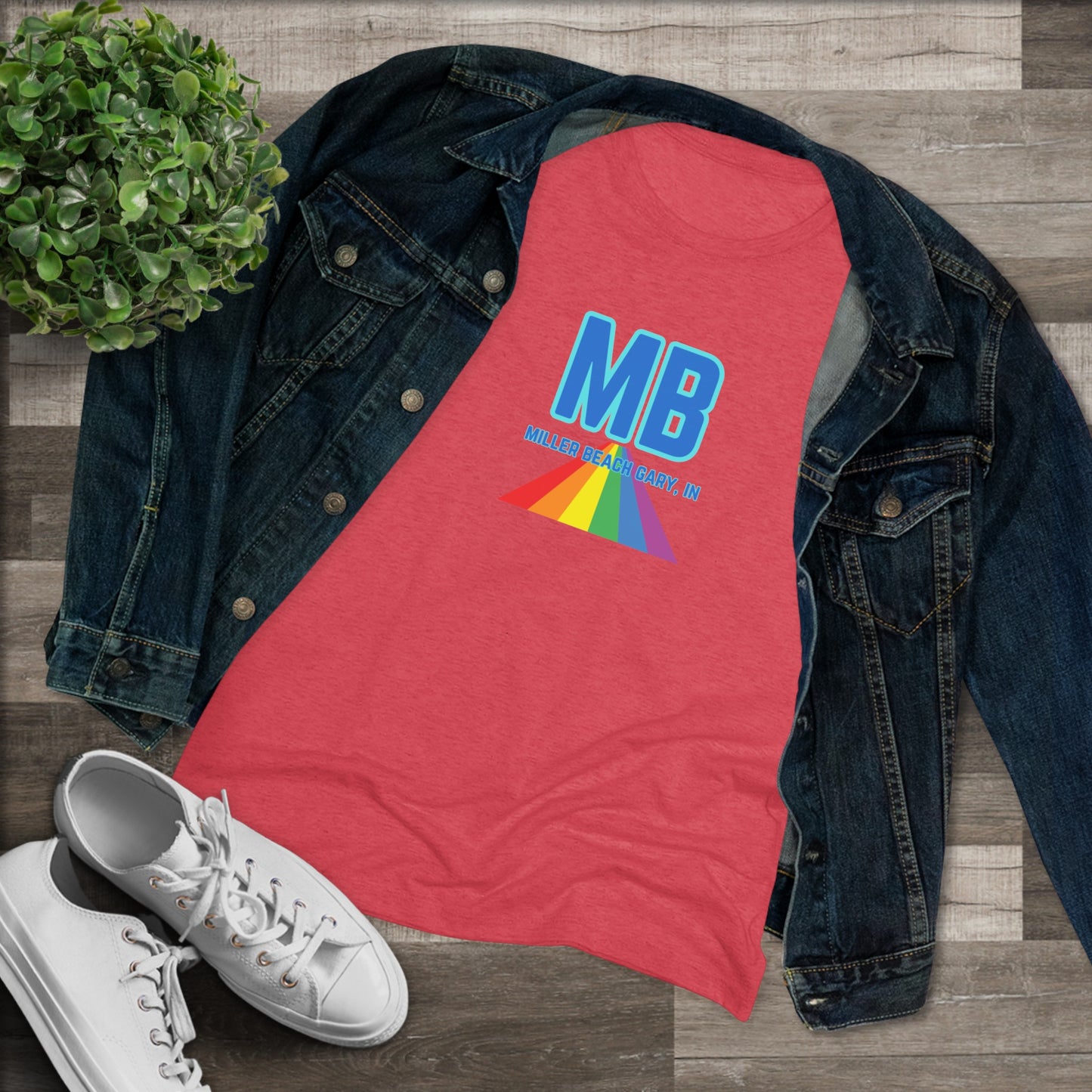 The Miller Beach Pride - Women's Triblend Tee by Printify is a dark gray, cozy t-shirt with a vintage look, featuring the text "MB" in large blue letters at the center. Below the letters, there is a rainbow-colored triangular design with "Millions & Binary, Inc." written in smaller text under the rainbow triangle.