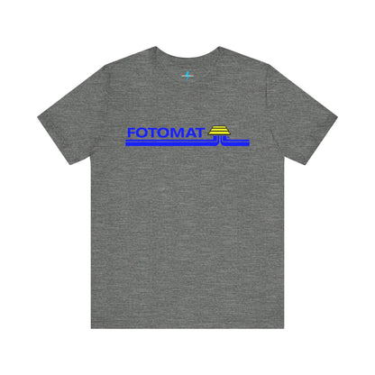 The Fotomat 1970s Retro T-Shirt by Printify is a dark gray short-sleeve shirt that features the word "FOTOMAT" in bold blue capital letters and a blue and yellow graphic design resembling layered lines and an upside-down triangle. This Tshirt captures the essence of 80s nostalgia with its centered, retro design.