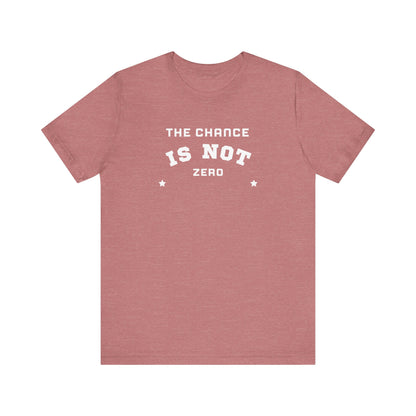 Folded light red Unisex Jersey Short Sleeve Tee from Printify, featuring bold white text that reads "THE CHANCE IS NOT ZERO" along with two star illustrations. This motivational T-shirt, made from breathable fabric, is neatly stacked with another identical shirt underneath.