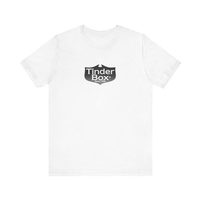 A light blue Printify "The Tinder Box 1980s" unisex jersey short sleeve tee featuring the "Tinder Box" logo in the center. The logo consists of a dark shield with the words "Tinder Box" in white text, with a small flame icon replacing the dot above the "i".