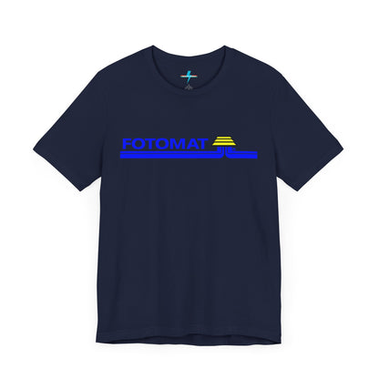 The Fotomat 1970s Retro T-Shirt by Printify is a dark gray short-sleeve shirt that features the word "FOTOMAT" in bold blue capital letters and a blue and yellow graphic design resembling layered lines and an upside-down triangle. This Tshirt captures the essence of 80s nostalgia with its centered, retro design.