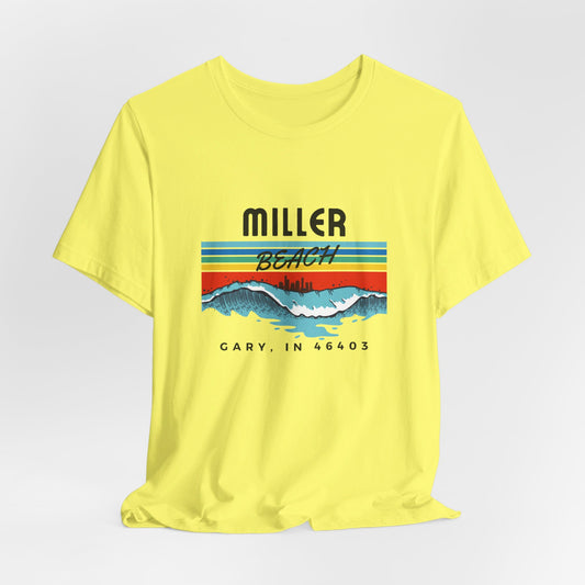 The Miller Beach 46403 Surf Style - Unisex Jersey Short Sleeve Tee by Printify features a retro surf-inspired design on a yellow background. The shirt displays "MILLER BEACH" above waves with a skyline illustration, while "Cary, IN 46403" is printed below the waves. The vibrant design also includes colorful stripes in shades of blue, red, and orange.