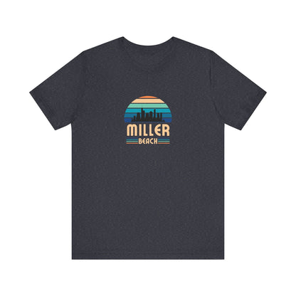 A brown unisex jersey short sleeve tee called "Miller Beach Chicago Skyline" from Printify features a vintage-style design with a sunset, the Chicago skyline, and "Miller Beach" in bold letters. The design incorporates shades of blue, orange, and yellow and is displayed against a plain white background.