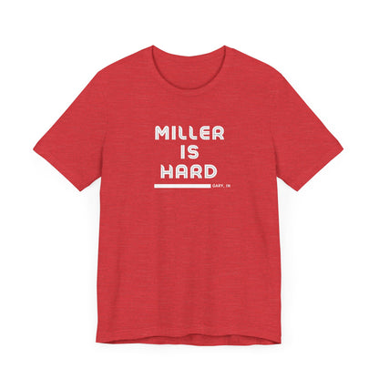 The Miller is Hard - White Letters - Unisex Jersey Short Sleeve Tee by Printify features a rust-colored design with "MILLER IS HARD" printed in bold, white capitals on the front. Below, "GARY, IN." is added in smaller font. This simple yet striking shirt evokes the spirit of Miller Beach with no additional graphics or patterns.