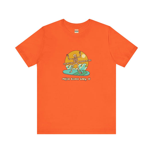 Introducing the Printify Miller Beach Skeleton on Paddle Board Unisex Jersey Short Sleeve Tee: a bright orange T-shirt crafted from soft cotton using sustainable manufacturing. It features a graphic of two dancing skeletons with a sun and waves in the background, accompanied by the text "Drop Me Off in Paradise by the Sea, Miller Beach Gary, IN.