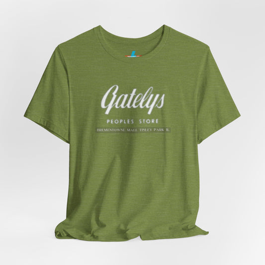 A green unisex jersey short sleeve tee from Printify's SoCool Shirts collection, featuring "Gately's People's Store" printed prominently in white on the front. Below this, smaller text reads "Tinley Park's Brementowne Mall" in white. The T-shirt is displayed against a plain white background and is named the "Gatelys Peoples Store - Vintage 1980s.