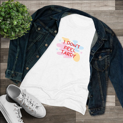 A light gray, short-sleeved Women's Triblend Tee from Printify with the playful phrase "I DON'T FEEL TARDY" printed in colorful letters on the front. The text is surrounded by abstract pastel shapes, giving it retro vibes and a vintage look reminiscent of a Van Halen T-shirt.