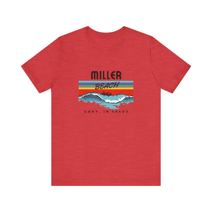 The Miller Beach 46403 Surf Style - Unisex Jersey Short Sleeve Tee by Printify features a retro surf-inspired design on a yellow background. The shirt displays "MILLER BEACH" above waves with a skyline illustration, while "Cary, IN 46403" is printed below the waves. The vibrant design also includes colorful stripes in shades of blue, red, and orange.